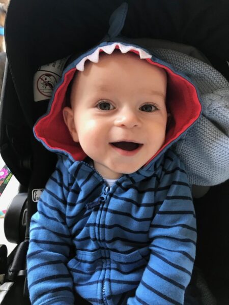 smiling infant in blue shirt and hat looking at the camera.