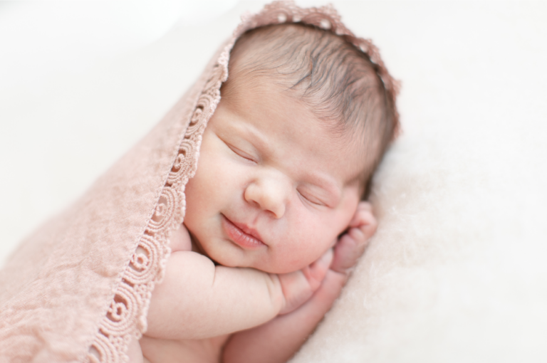 Close up image of a new born baby sleeping on their site with a baby blanket covering the head.