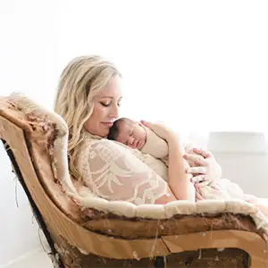 A new mom holding a sleeping infant lovingly to her chest while sitting in a chair.