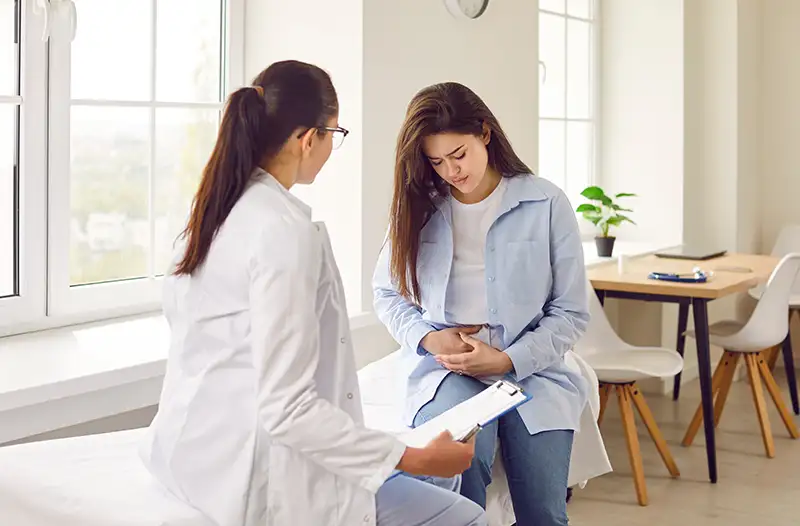 Young woman clutching her lower abdomen in pain sitting across from a female healthcare provider.